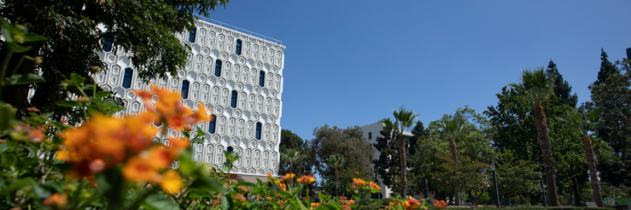 Banner image of Pollak Library building with flowers in the foreground and trees in the background